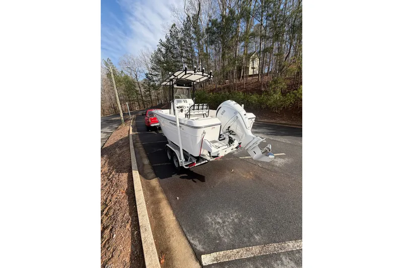 Slide: The Image of 2024 Aquasport 2100 Center Console boat on trailer, parked near trees. - 6