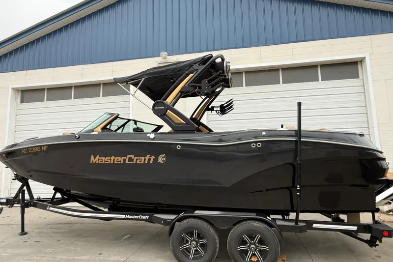 The Image of 2025 MasterCraft X24 boat on trailer, sleek black design, parked outside a garage. - 0