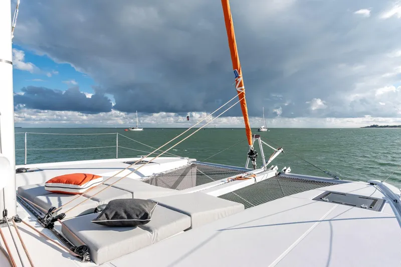 Slide: The Image of Luxurious 2022 Excess 11 catamaran deck with cushions, sailing on calm waters under cloudy skies. - 20