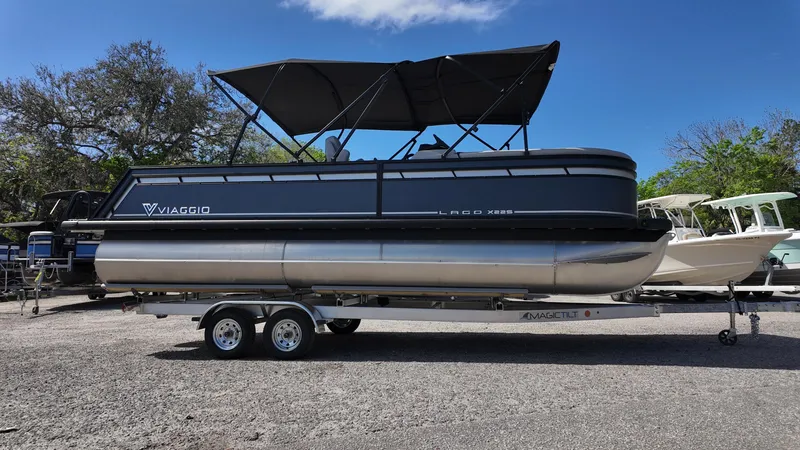 Slide: The Image of 2025 Viaggio X22S pontoon boat on trailer, parked outdoors under clear blue sky. - 2