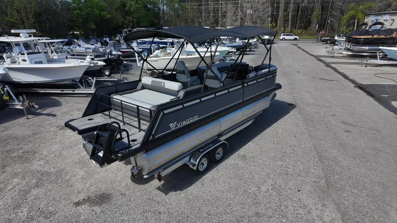 Slide: The Image of 2025 Viaggio X22S pontoon boat with canopy, parked on a trailer in a marina. - 3