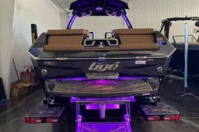 Slide: The Image of 2025 Tigé Ultré 25ZX boat with illuminated deck and sleek design in a showroom. - 2