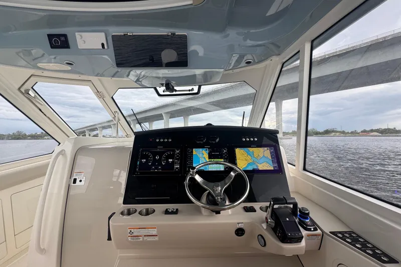 Slide: The Image of 2018 Boston Whaler 380 Realm helm with navigation screens, steering wheel, and water view. - 15