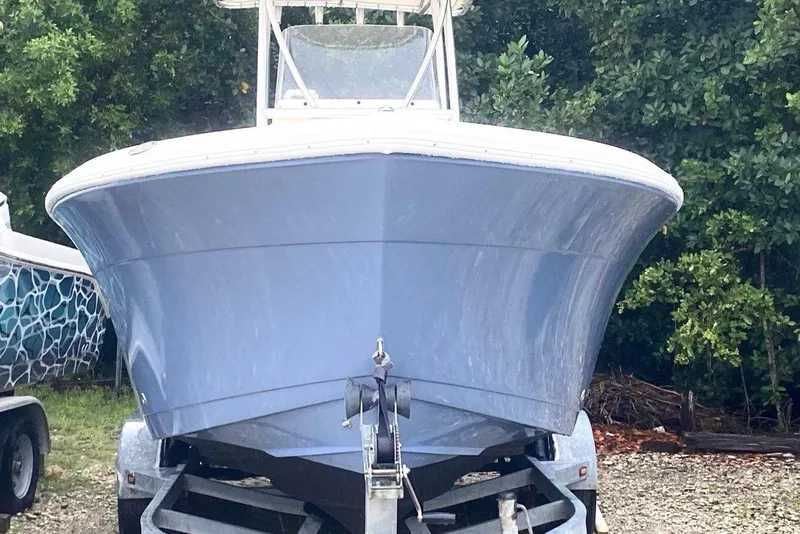 Slide: The Image of 2019 Cobia 220 Center Console boat on trailer, front view, surrounded by greenery. - 1