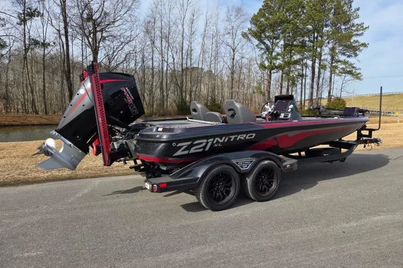 Slide: The Image of 2022 Nitro Z21 XL boat on trailer, parked near trees and water. - 2