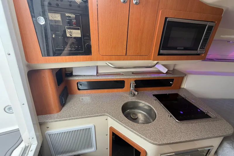 Slide: The Image of 2010 Triton 351 Express boat kitchen with sink, stove, microwave, and wooden cabinets. - 34
