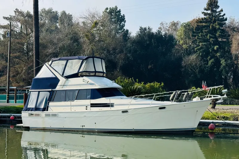 The Image of 1990 Bayliner 3888 Motoryacht docked on calm water, surrounded by trees. - 0