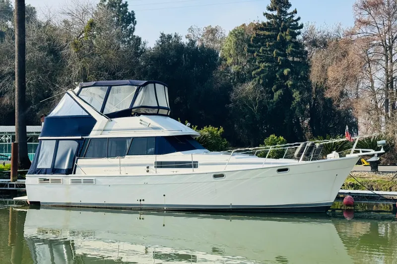 Slide: The Image of 1990 Bayliner 3888 Motoryacht docked on calm water, surrounded by trees. - 4