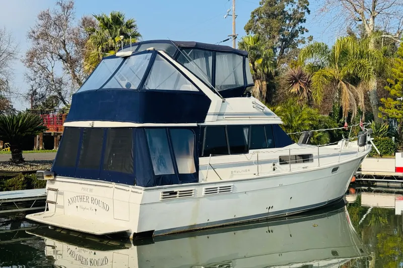 Slide: The Image of 1990 Bayliner 3888 Motoryacht docked, featuring blue canopy and lush surroundings. - 7