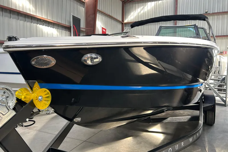 Slide: The Image of 2026 Four Winns H2 boat in showroom, black hull with blue stripe, on trailer. - 12