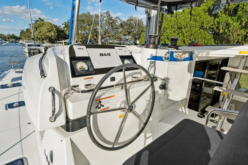 The Image of Steering wheel and controls of a 2020 Lagoon 42 catamaran, docked by a scenic waterway. - 0