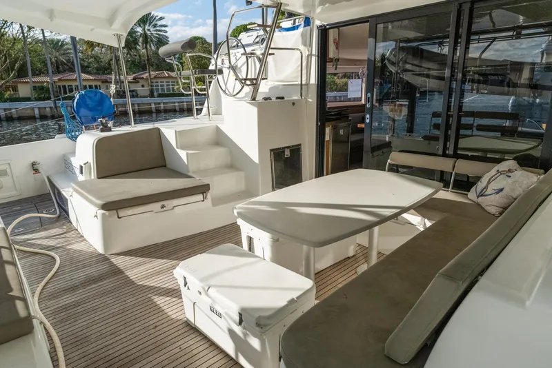 Slide: The Image of 2020 Lagoon 42 yacht cockpit with seating, table, and helm station, docked by waterfront homes. - 6