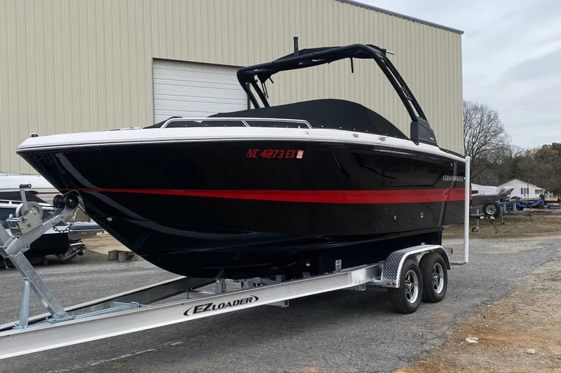 The Image of 2022 Chaparral 247 SSX boat on trailer, black with red stripe, parked outdoors. - 0