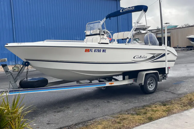 Slide: The Image of 2003 Cobia 184 Center Console boat on trailer, parked near blue building. - 6