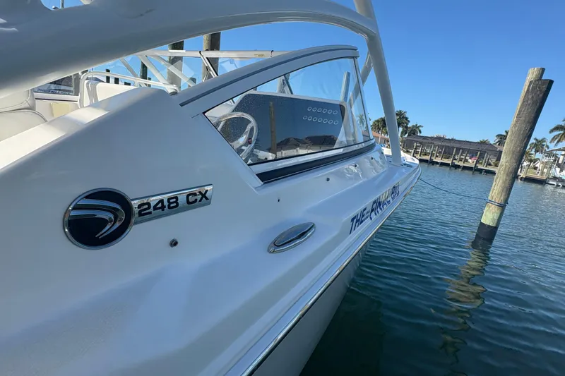 Slide: The Image of 2023 Edgewater 248CX Crossover boat interior at marina, featuring white seating and sleek design. - 18