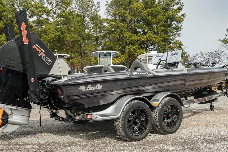 Slide: The Image of 2023 Bass Cat Puma STS boat with dual axle trailer, parked outdoors. - 2