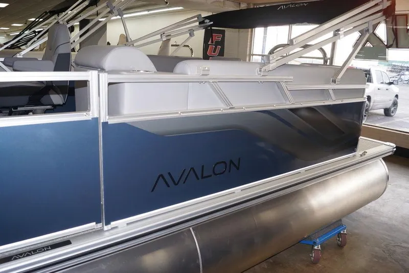 Slide: The Image of 2026 Avalon VLS Quad Lounge 21' pontoon boat in showroom, side view. - 3