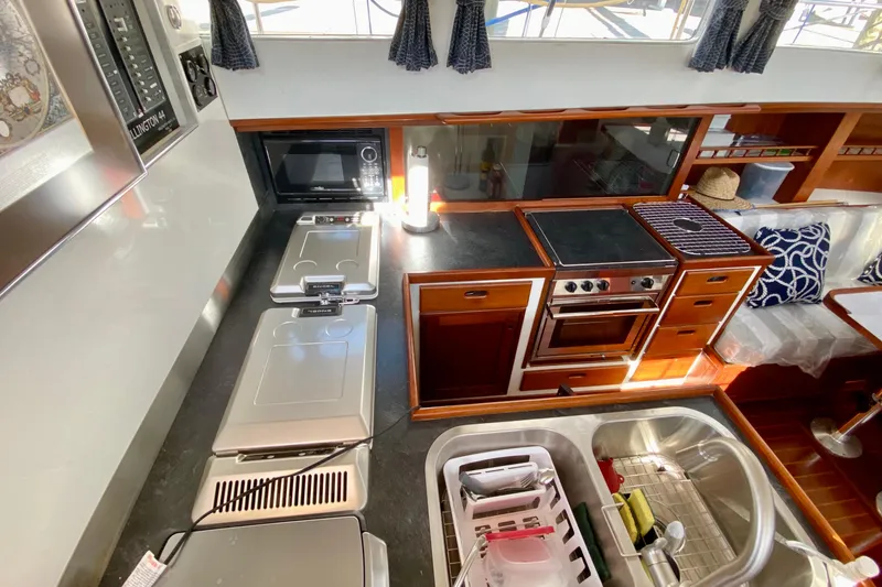 Slide: The Image of 1980 Wellington 44 yacht kitchen with stove, microwave, and sink, featuring wooden cabinetry and modern appliances. - 22