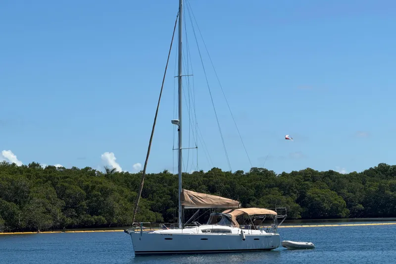Slide: The Image of 2008 Beneteau Oceanis 40 sailboat anchored near lush green shoreline under clear blue sky. - 48