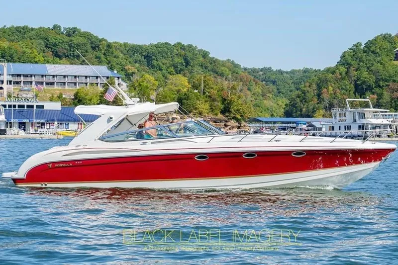 The Image of 2003 Formula 400 Super Sport boat cruising on a scenic lake with lush greenery. - 1