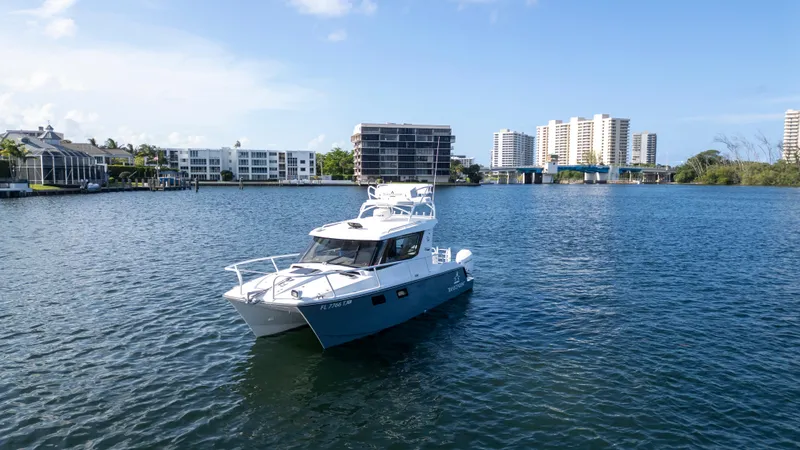 Slide: The Image of 2023 ArrowCat Flybridge Dual Helm boat on a serene waterway with cityscape backdrop. - 1