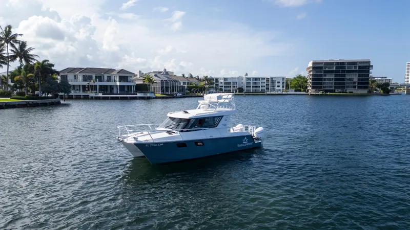 Slide: The Image of 2023 ArrowCat Flybridge Dual Helm boat on a calm waterway with modern buildings in the background. - 9