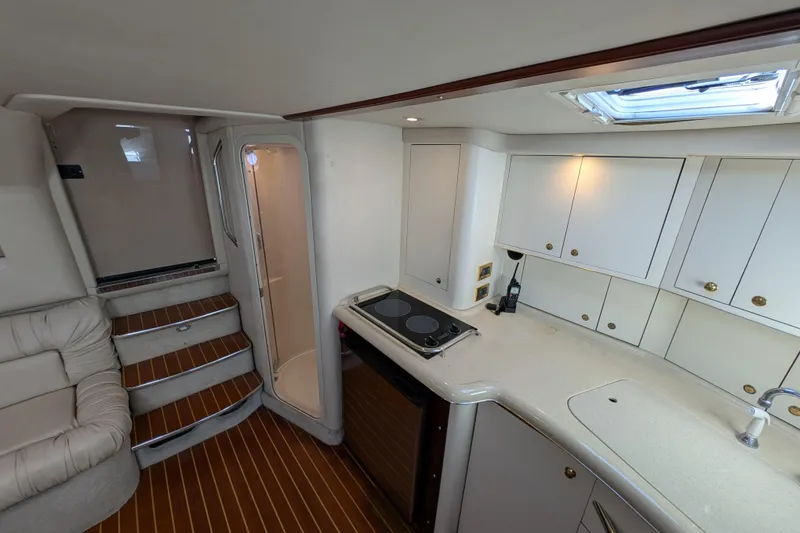 Slide: The Image of 1999 Sea Ray 370 Express Cruiser interior with kitchenette, stairs, and seating area. - 27