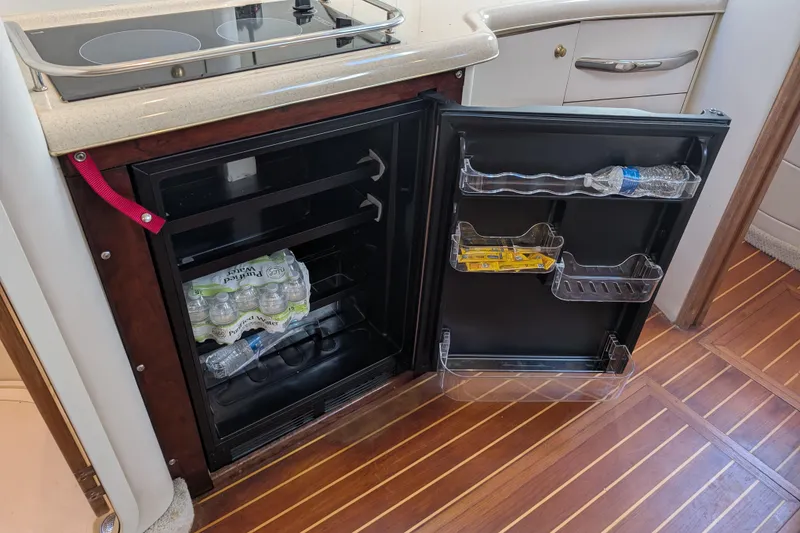 Slide: The Image of 1999 Sea Ray 370 Express Cruiser galley with open fridge, stocked with water bottles and snacks. - 31