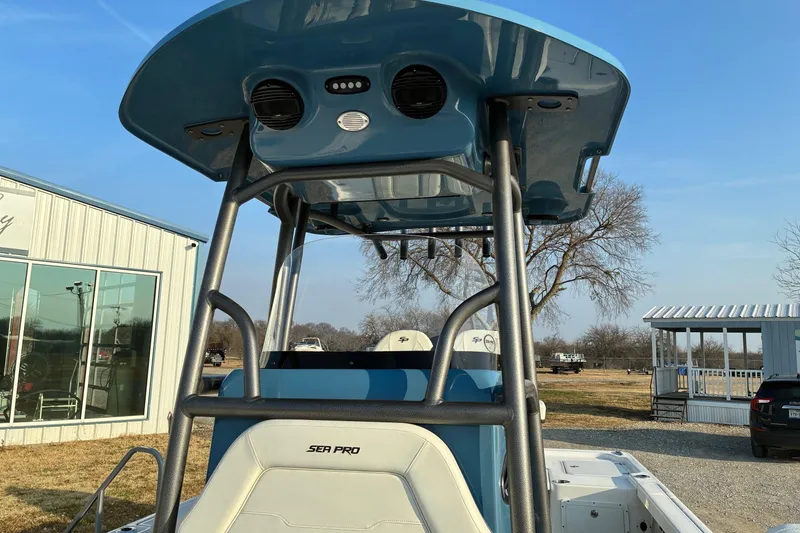 Slide: The Image of 2026 Sea Pro 250 Bay boat with blue T-top and white seating, parked outdoors. - 11