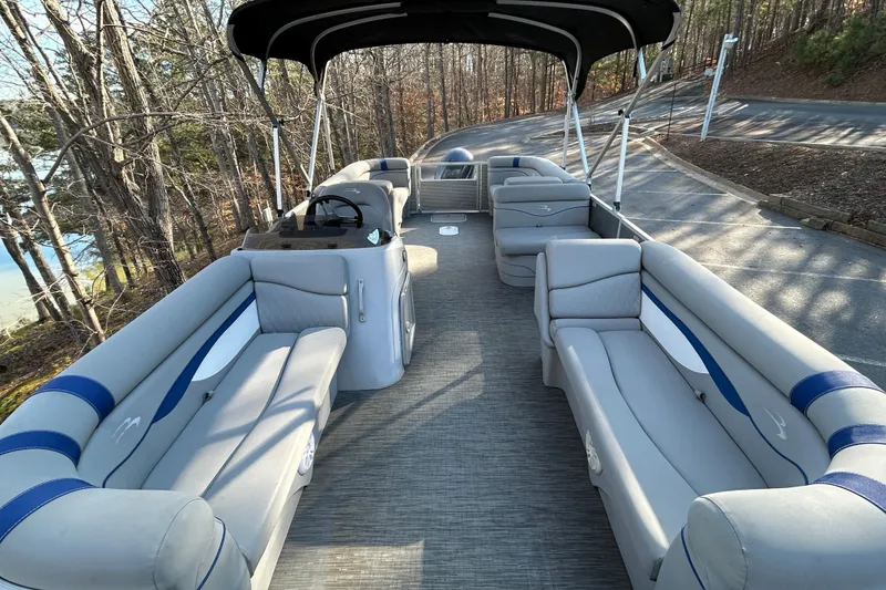 Slide: The Image of 2023 Bennington 22 SSRX pontoon boat with spacious seating and canopy, parked near a wooded area. - 8