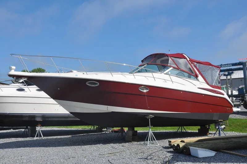 The Image of 2006 Monterey 322 Cruiser boat on stands, red and white hull, docked on gravel. - 0