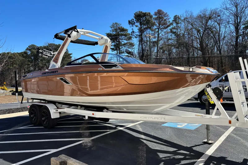 Slide: The Image of 2022 Centurion Ri245 boat on trailer, parked outdoors, surrounded by trees. - 2