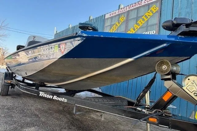 Slide: The Image of 2008 Triton TC-17 boat on trailer, parked near blue fence with Sizzle Marine sign. - 3
