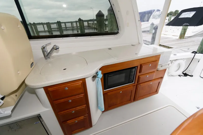 Slide: The Image of 2010 Back Cove 33 yacht interior with kitchenette, featuring sink, microwave, and wooden cabinetry. - 13