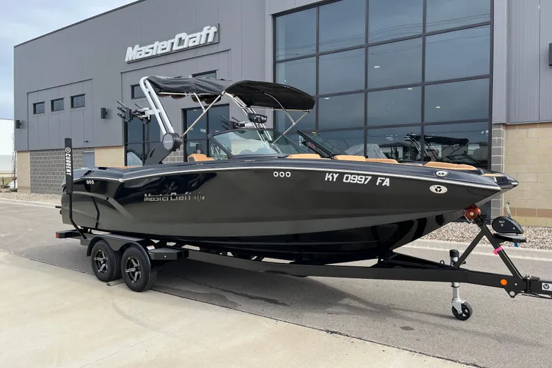 The Image of 2023 MasterCraft NXT24 boat on trailer outside dealership building. - 1