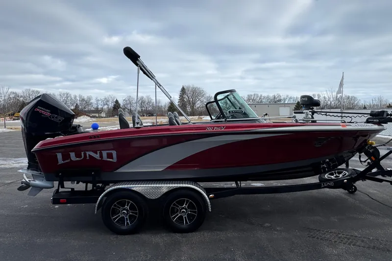 Slide: The Image of 2022 Lund 202 Pro-V GL boat on trailer, parked outdoors under cloudy sky. - 1