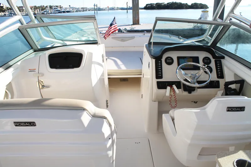 Slide: The Image of 2016 Robalo R247 Dual Console boat interior with steering wheel and seating, docked by the water. - 15