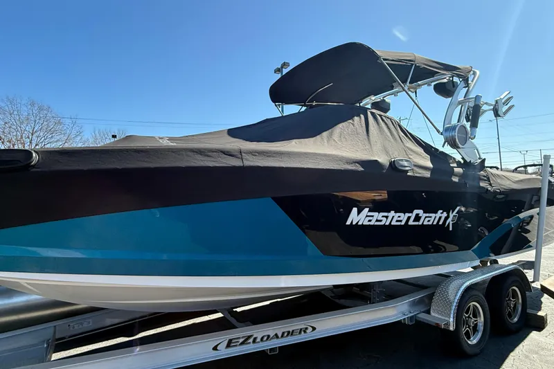 The Image of 2018 MasterCraft X26 boat on trailer, covered, with blue and black design. - 0