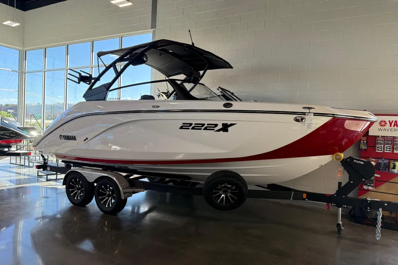The Image of 2026 Yamaha Boats 222XD in showroom, sleek white and red design on trailer. - 21