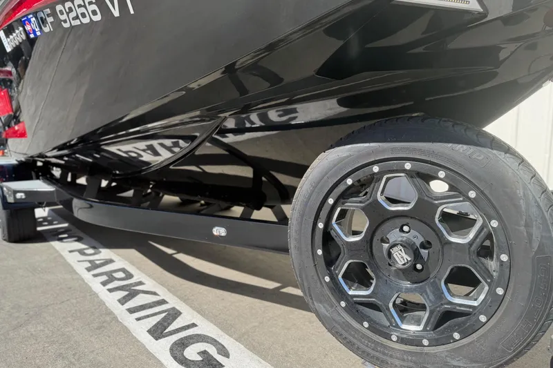 Slide: The Image of 2021 Malibu Wakesetter 23 MXZ boat on trailer, close-up of black wheel and hull. - 3