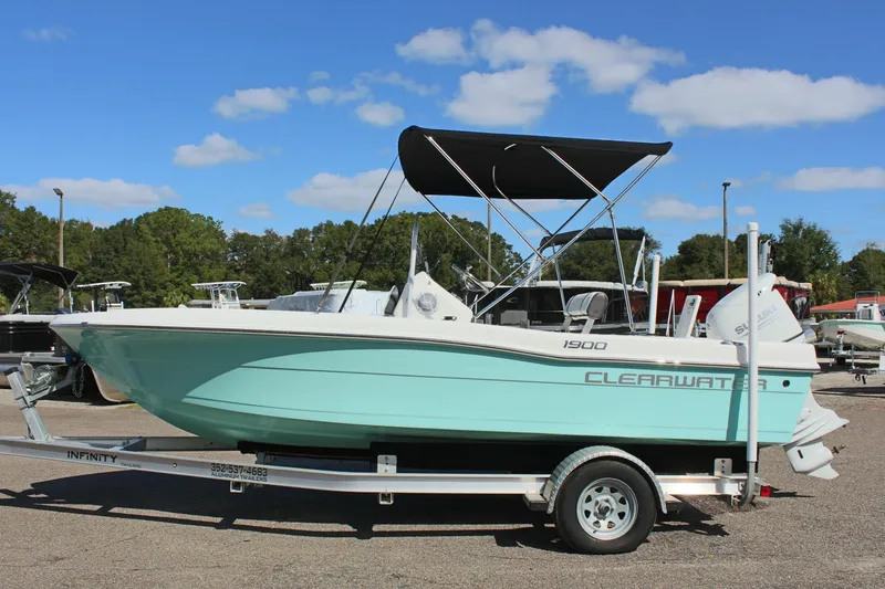 The Image of 2024 Clearwater 1900 CC boat on trailer, mint green hull, black canopy, outdoor setting. - 1