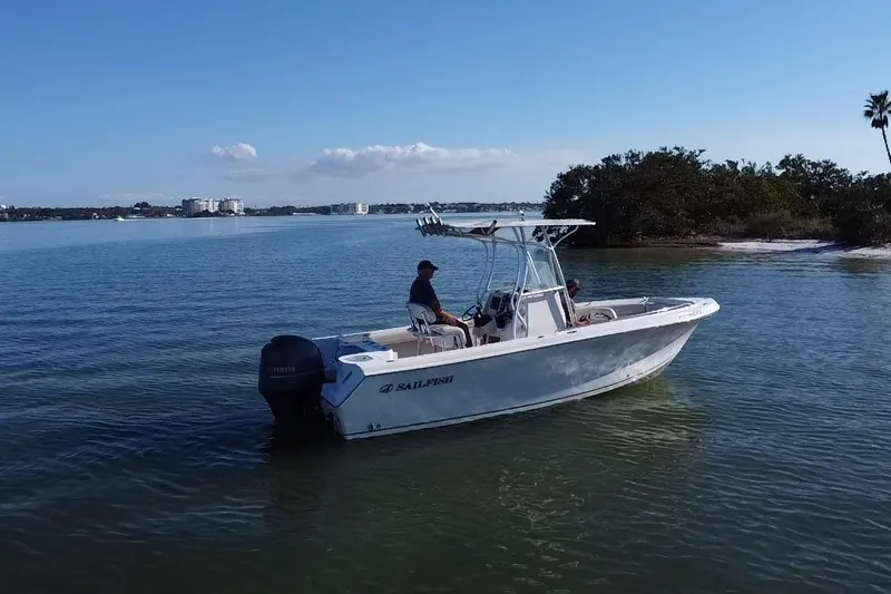 Slide: The Image of 2015 Sailfish 220 CC boat on calm water near shoreline, clear sky background. - 20