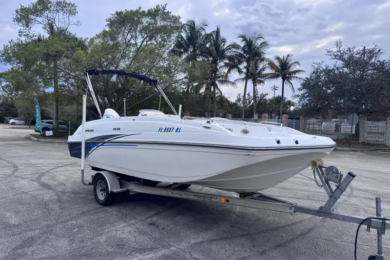 Slide: The Image of 2018 Hurricane SunDeck Sport 188 OB boat on trailer, parked near palm trees. - 2