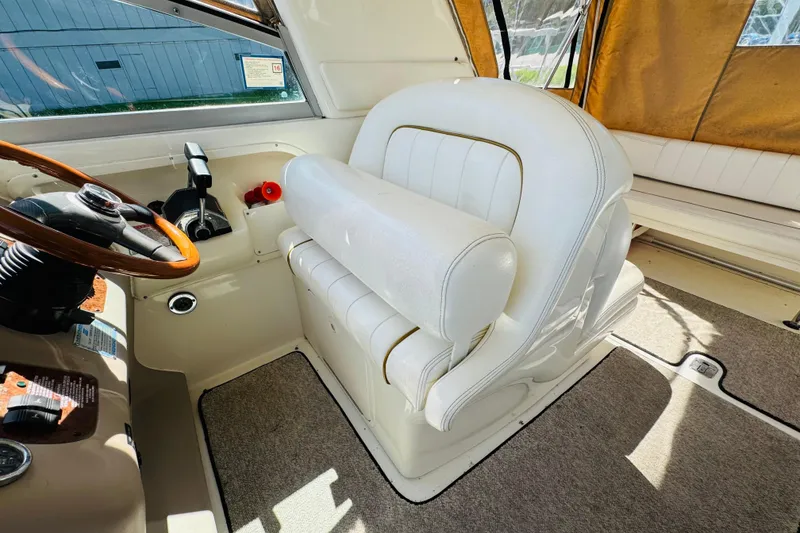 Slide: The Image of Captain's seat and helm of 2000 Sea Ray 290 Sundancer boat, featuring white upholstery and wooden steering wheel. - 29