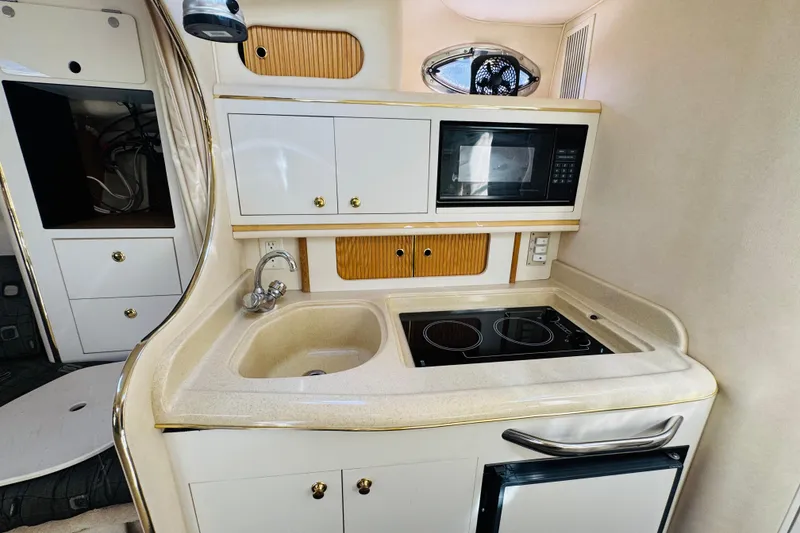 Slide: The Image of Compact kitchen area in a 2000 Sea Ray 290 Sundancer boat, featuring sink, stove, and microwave. - 36
