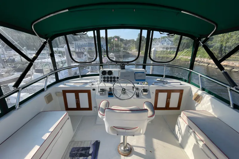 Slide: The Image of 1987 Heritage East 40 Sundeck helm with panoramic marina view, featuring classic controls and seating. - 7