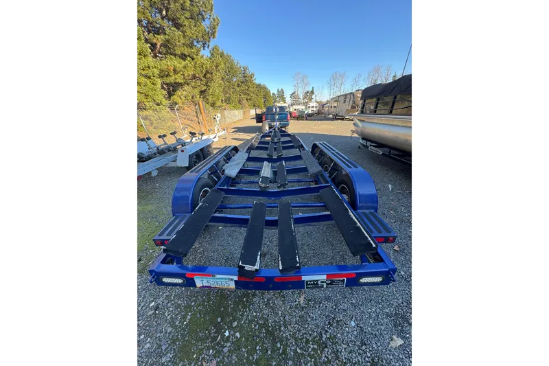 Slide: The Image of Blue boat trailer for 2008 Intrepid 327, parked on gravel lot with trees in background. - 32