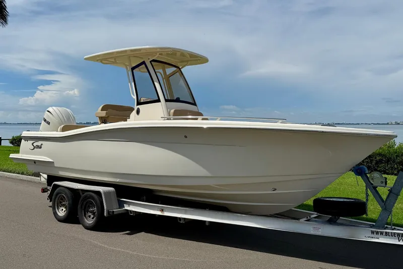 Slide: The Image of 2025 Scout 240 XSF boat on trailer by waterfront, under clear sky. - 2