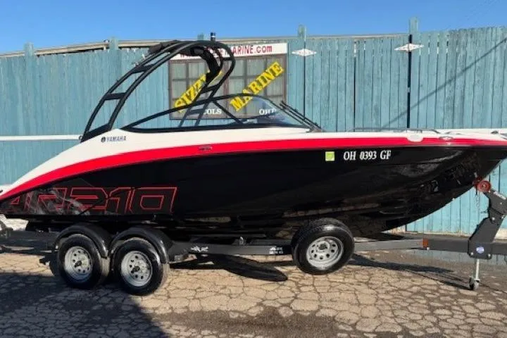 The Image of 2021 Yamaha AR210 boat on trailer, black and red design, parked outdoors. - 0