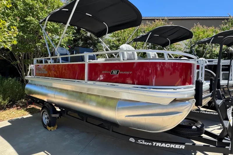 Slide: The Image of 2026 Sun Tracker Bass Buggy 18 DLX pontoon boat on trailer, parked outdoors. - 2